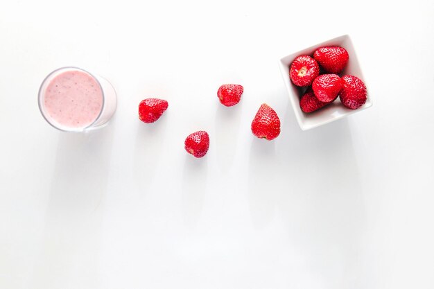 Vista plana mínima de batido de fresa y fresas sobre fondo blanco con espacio de copia