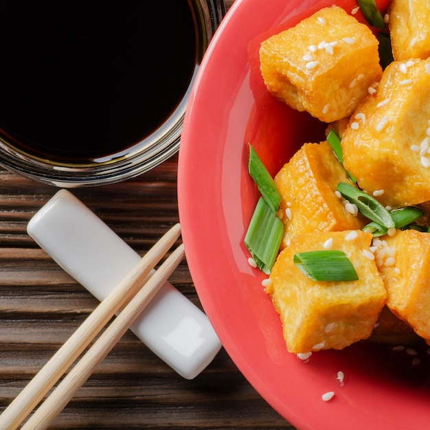 Vista plana de primer plano en trozos de tofu frito crujiente con cebollino y sésamo en plato de arcilla