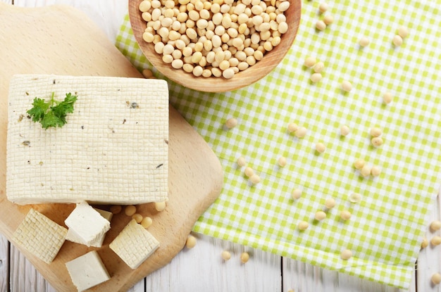 Vista plana en el tofu de cuajada de soja en la tabla de cortar con un tazón de frijoles a un lado Sustituto alternativo no lácteo del queso