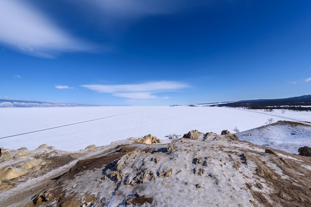 Vista a la playa de sarai desde el cabo burhan en la isla de olkhon en día soleado de invierno. el lago baikal congelado cubierto de nieve. hermoso estrato de nubes sobre la superficie del hielo en un día helado.