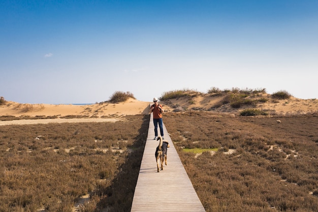 Vista por trás de um homem caminhando com seu cachorro em uma estrada que conduz a uma bela paisagem.