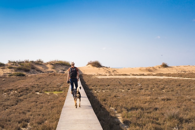 Vista por trás de um homem caminhando com seu cachorro em uma estrada que conduz a uma bela paisagem.