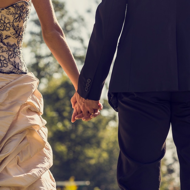 Vista por trás do casal recém-casado, noiva e noivo, de mãos dadas do lado de fora em um dia ensolarado, efeito retro desbotado olhar.