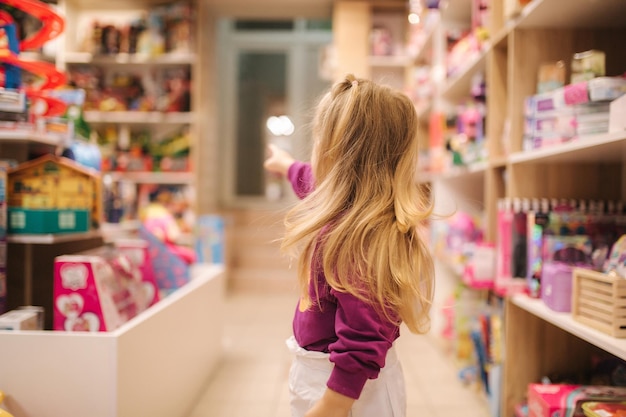 Vista posterior de la adorable niña comprando juguetes linda mujer en la tienda de juguetes niña feliz