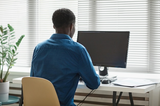 Foto vista posterior al hombre afroamericano usando la computadora en el escritorio por espacio de copia de ventana