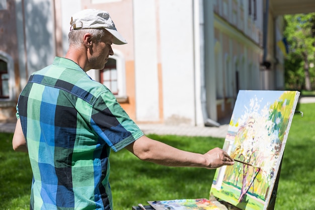 Vista posterior de un artista masculino que trabaja al aire libre en el parque o jardín