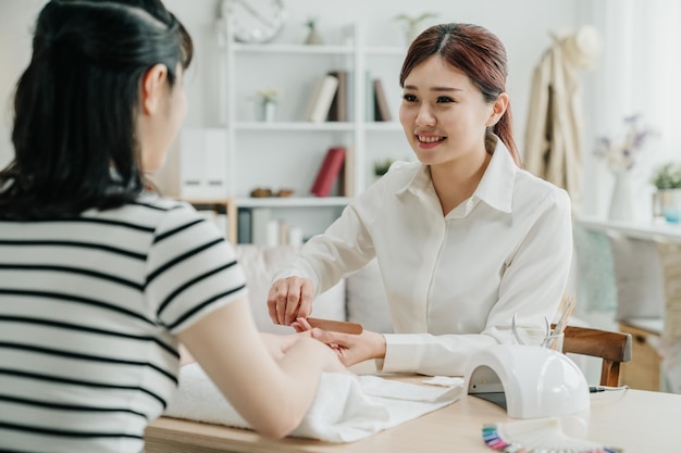 vista posterior de una clienta en casa recibiendo manicura por una esteticista sonriente con lima de uñas. amable manicurista lima las uñas a la señora clienta. elegante especialista en uñas que trabaja en una casa de huéspedes.