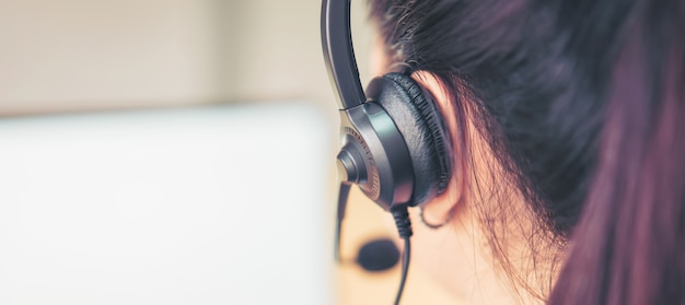 Vista posterior del consultor de la mujer con auriculares con micrófono del operador de telefonía de atención al cliente en el lugar de trabajo.