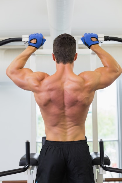 Vista posterior de un culturista masculino haciendo pull ups en el gimnasio