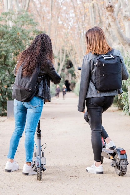 Vista posterior de dos amigas multiétnicas en scooters eléctricos. estilo de vida urbano