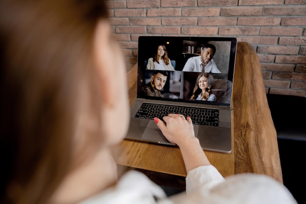 Vista posterior de una empleada que tiene una conferencia en línea con colegas usando una computadora portátil joven