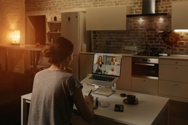 Vista posterior de una empleada que trabaja de forma remota y habla con sus colegas en una videoconferencia en una computadora portátil desde casa.