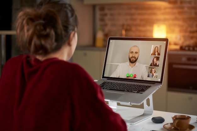 Vista posterior de una empleada que trabaja de forma remota hablando con su colega sobre negocios en una videoconferencia en una computadora portátil en casa.