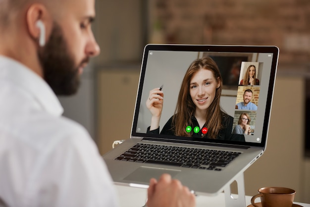 Foto vista posterior de un empleado masculino calvo con barba que está escuchando a un colega en una videoconferencia.