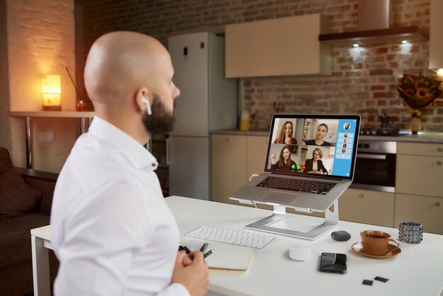 Vista posterior de un empleado que trabaja de forma remota en una videoconferencia empresarial en una computadora portátil en casa.