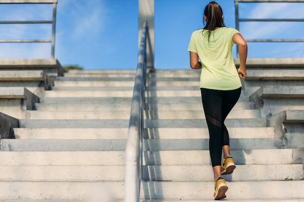 Vista posterior de la enérgica joven morena vestida con camiseta amarilla y pantalón negro para correr en los escalones.