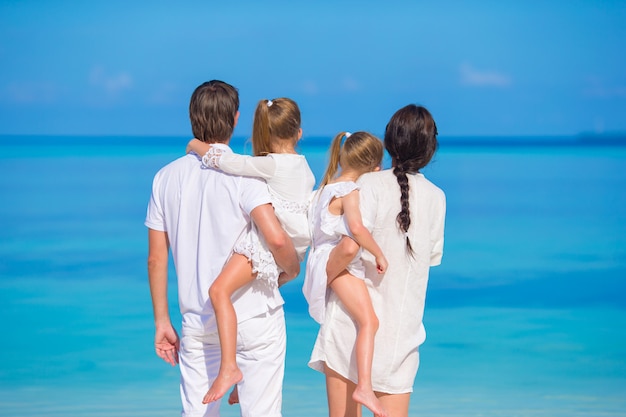 Vista posterior de una familia de cuatro jóvenes en la playa blanca durante las vacaciones de verano