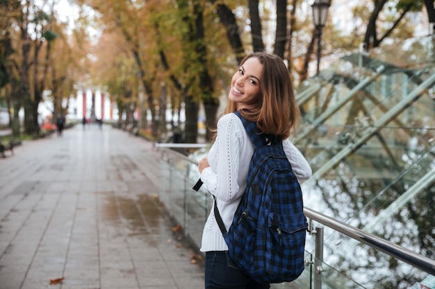 Vista posterior de la feliz mujer joven y bonita con mochila caminando en el parque