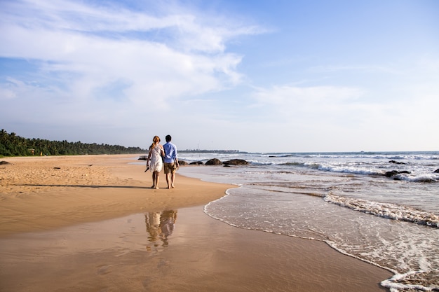 Vista posterior de la feliz pareja joven caminando en una playa tropical desierta. foto tonificante