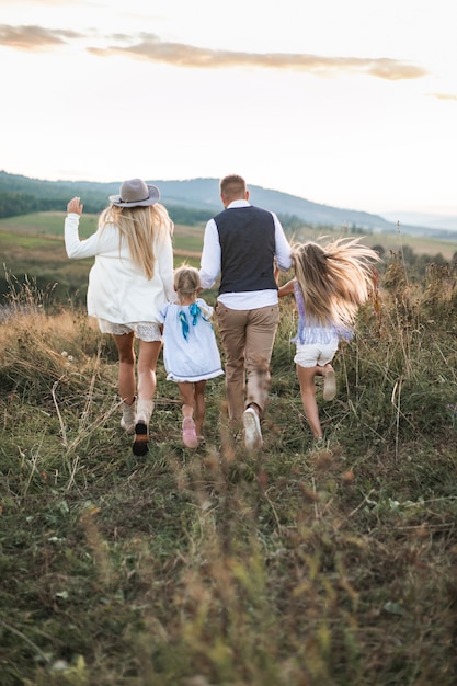 Vista posterior de la foto de una familia alegre con ropa elegante de moda, padres e hijos, disfrutando y corriendo juntos en las montañas
