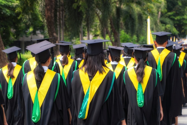 Vista posterior del grupo de graduados universitarios en vestidos negros se alinea para obtener el título en la ceremonia de graduación universitaria.
