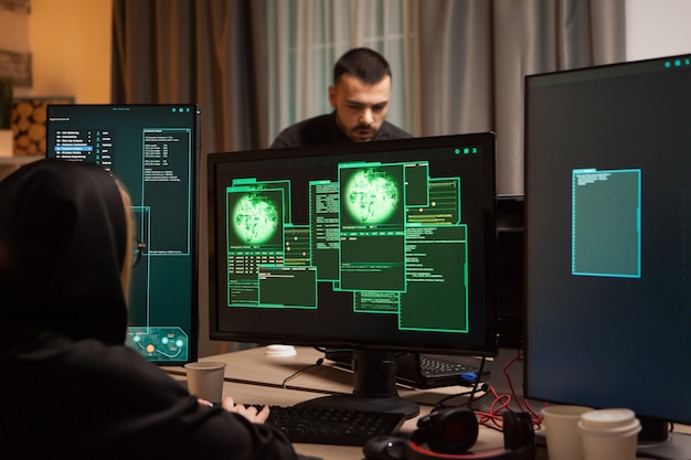Foto vista posterior de una hacker escribiendo un malware malicioso y un ciber terrorista en segundo plano.
