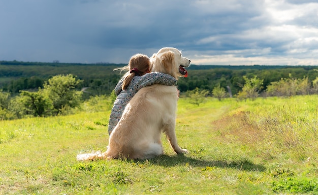 Vista posterior de la hermosa niña abrazando a un perro leal en la naturaleza