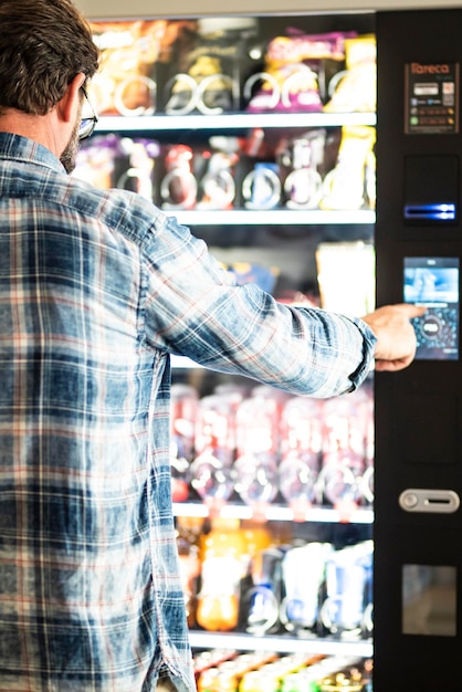 Vista posterior de un hombre adulto maduro que elige bocadillos y bebidas en un distribuidor automático gratuito las 24 horas personas que compran alimentos en la puerta del aeropuerto estilo de vida de viaje y nutrición basura estilo de vida poco saludable