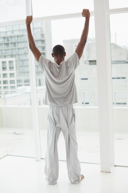 Vista posterior del hombre afro estirando sus brazos cerca de la ventana