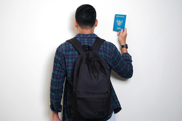 Vista posterior del hombre asiático adulto con mochila mostrando el pasaporte de Indonesia listo para viajar