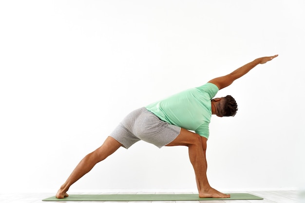 Vista posterior del hombre deportivo practicando yoga en clase de yoga haciendo estiramiento hacia atrás