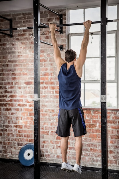 Foto vista posterior del hombre haciendo pull ups en el gimnasio