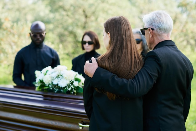 Foto vista posterior de un hombre maduro con traje negro abrazando a su afligida hija