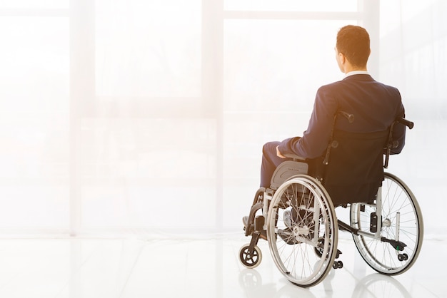 Vista posterior de un hombre de negocios sentado en silla de ruedas mirando a la ventana