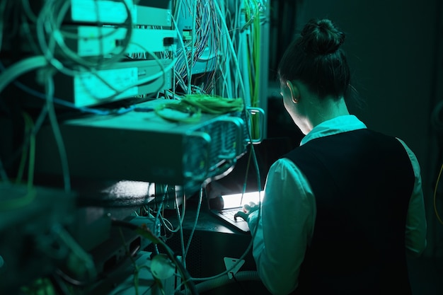 Vista posterior de la ingeniera de red femenina inspeccionando servidores mientras trabaja con una supercomputadora en el centro de datos, espacio de copia