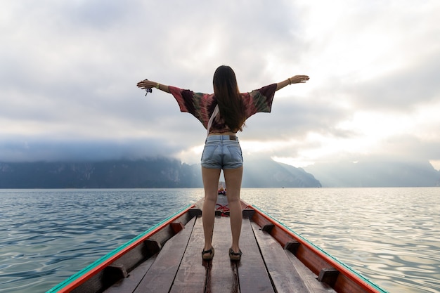 Vista posterior de la joven asiática viajando en barco de madera al amanecer entre la isla de Khao Sok, Tailandia
