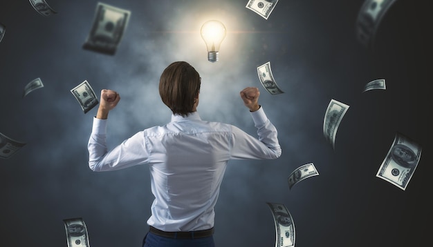 Foto vista posterior del joven empresario exitoso con lluvia de dinero de billete de dólar sobre fondo de pared oscura concepto de ganador de dinero y lotería de éxito