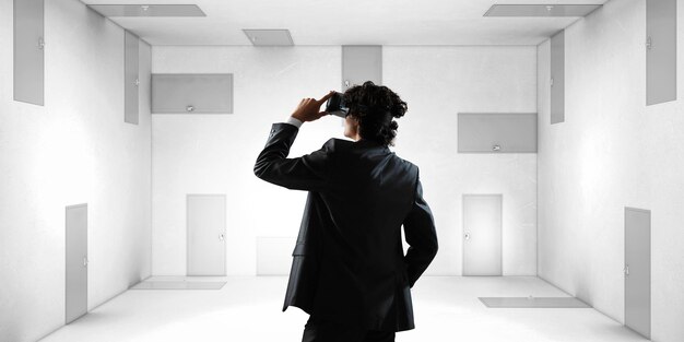 Foto vista posterior de un joven hombre de negocios con auriculares de realidad virtual en una habitación con muchas puertas. técnica mixta