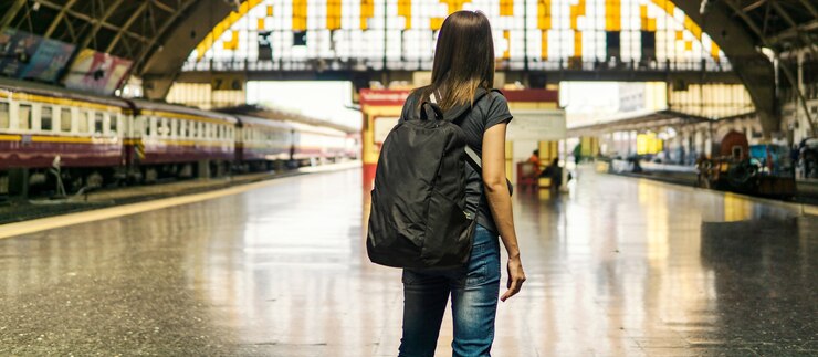 Vista posterior de la joven mujer asiática viajero con mochila pequeña en la estación de ferrocarril.Esperando el tren para el transporte en viaje de vacaciones.Concepto de viaje