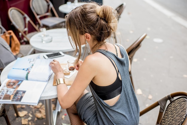 Vista posterior de la joven mujer elegante tomando café al aire libre en el café de París