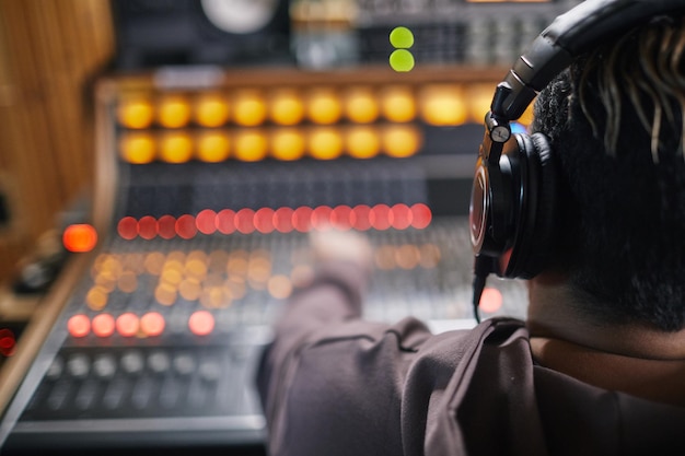 Vista posterior de un joven músico que usa auriculares en una estación de trabajo de audio en un estudio de grabación profesional