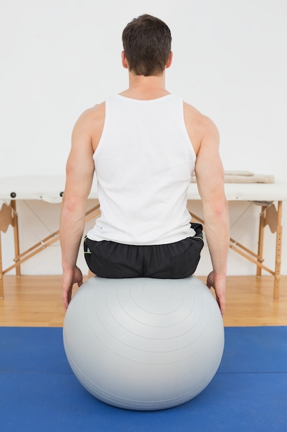 Vista posterior de un joven sentado en una pelota de yoga