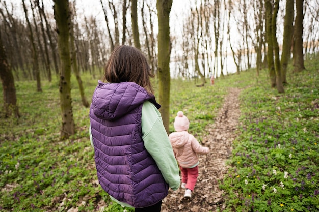 Vista posterior de la madre con la hija caminando por el sendero del bosque Concepto de ocio de primavera al aire libre