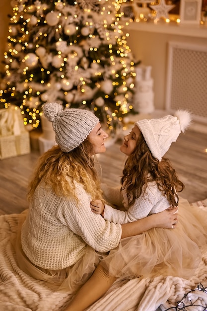 Vista posterior de la madre y la hija en sombreros de punto cerca del árbol de Navidad brillante, en el invierno para las vacaciones de Navidad