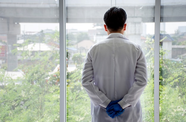 Foto vista posterior del médico asiático de pie con las manos juntas detrás de la espalda
