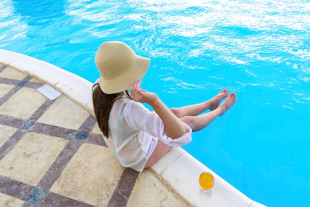 Vista posterior mujer adulta joven persona disfrutar relajándose en el borde de la piscina en un complejo hotelero de lujo al aire libre mirando el agua azul clara Concepto de turismo de vacaciones recreativas tropicales de viajes de verano
