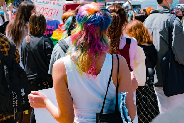 Vista posterior de una mujer joven con el color del arco iris del corte de pelo protestando en la calle Mano joven Ira Evento civil Lucha Movimiento Sociedad Estudiante Problemas sociales Protesta Cambio Banner