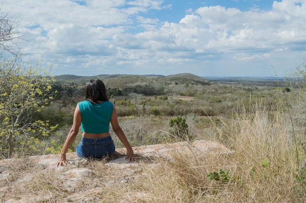 Vista posterior de una mujer joven mirando el horizonte desde las alturas de la colina