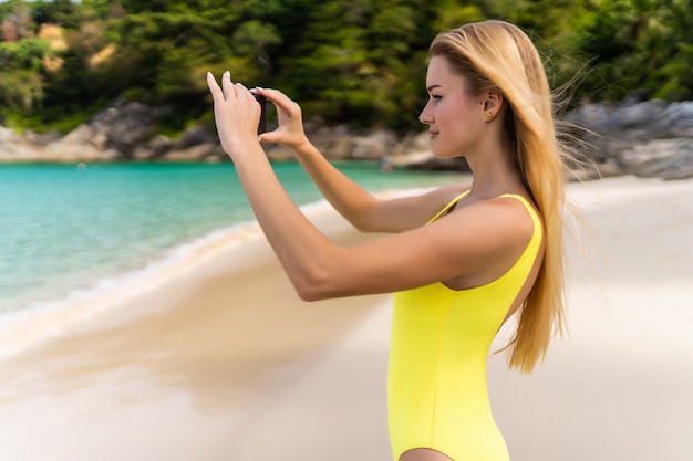 Vista posterior de una mujer joven que toma una fotografía con una cámara de teléfono inteligente en la playa