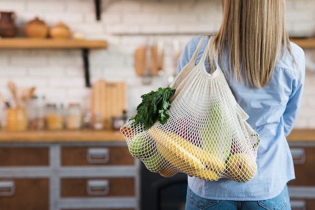 Vista posterior mujer llevando bolsa reutilizable con frutas orgánicas